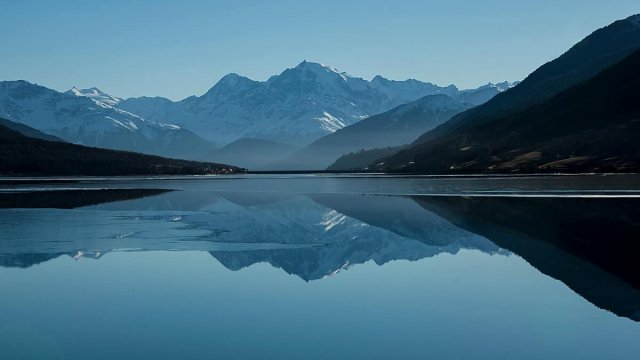 Snow-capped mountains reflected in a calm alpine lake Mountain lake reflecting snow-capped peaks under blue sky