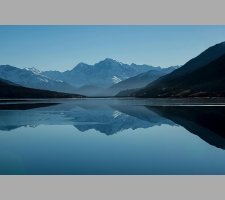 Snow-capped mountains reflected in a calm alpine lake Mountain lake reflecting snow-capped peaks under blue sky