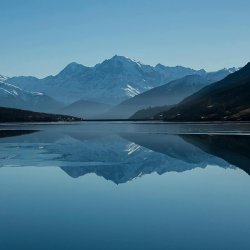 Mountain lake reflecting snow-capped peaks under blue sky
