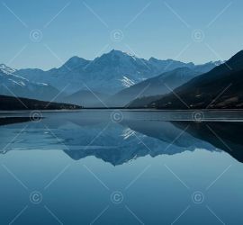Mountain lake reflecting snow-capped peaks under blue sky