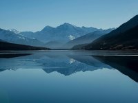 Snow-capped mountains reflected in a calm alpine lake Mountain lake reflecting snow-capped peaks under blue sky