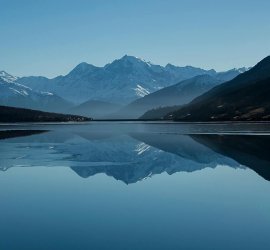 Snow-capped mountains reflected in a calm alpine lake Mountain lake reflecting snow-capped peaks under blue sky