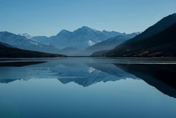 Snow-capped mountains reflected in a calm alpine lake Mountain lake reflecting snow-capped peaks under blue sky