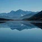 Snow-capped mountains reflected in a calm alpine lake Mountain lake reflecting snow-capped peaks under blue sky