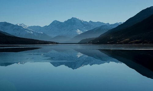 Snow-capped mountains reflected in a calm alpine lake Mountain lake reflecting snow-capped peaks under blue sky