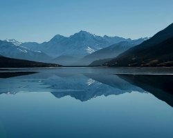 Snow-capped mountains reflected in a calm alpine lake Mountain lake reflecting snow-capped peaks under blue sky