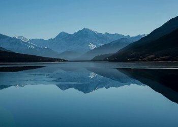 Snow-capped mountains reflected in a calm alpine lake Mountain lake reflecting snow-capped peaks under blue sky