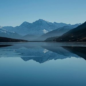 Snow-capped mountains reflected in a calm alpine lake Mountain lake reflecting snow-capped peaks under blue sky