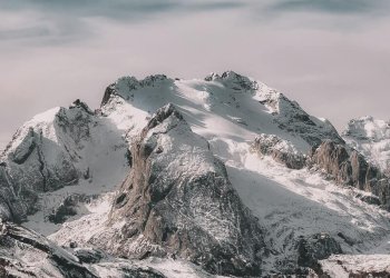 Snow-covered mountain range under cloudy sky Snowy mountain peaks with cloudy sky