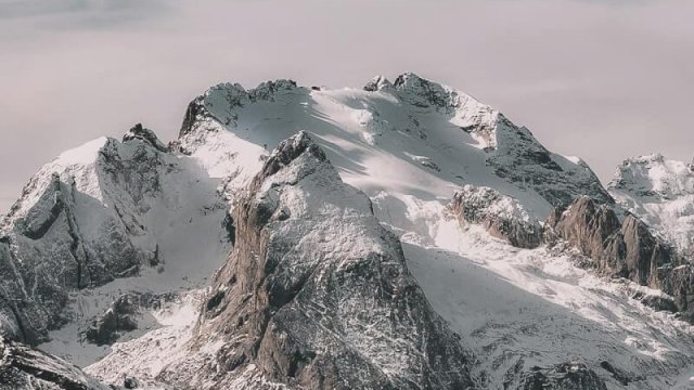 Snow-covered mountain range under cloudy sky Snowy mountain peaks with cloudy sky