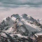 Snow-covered mountain range under cloudy sky Snowy mountain peaks with cloudy sky