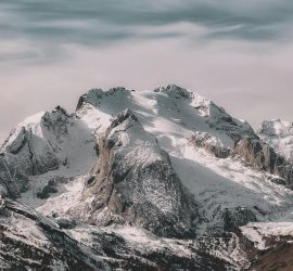 Snow-covered mountain range under cloudy sky Snowy mountain peaks with cloudy sky