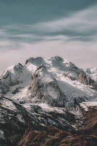 Snow-covered mountain range under cloudy sky Snowy mountain peaks with cloudy sky