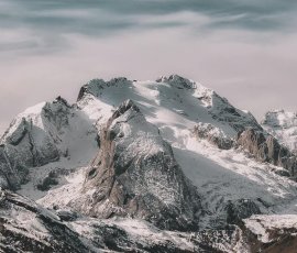 Snow-covered mountain range under cloudy sky Snowy mountain peaks with cloudy sky