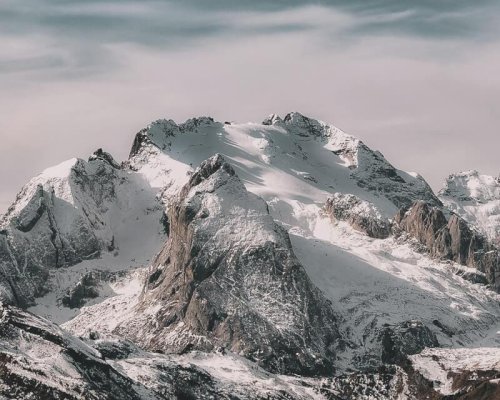 Snow-covered mountain range under cloudy sky Snowy mountain peaks with cloudy sky