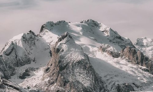 Snow-covered mountain range under cloudy sky Snowy mountain peaks with cloudy sky