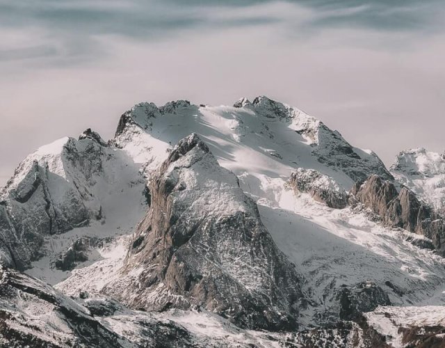 Snow-covered mountain range under cloudy sky Snowy mountain peaks with cloudy sky