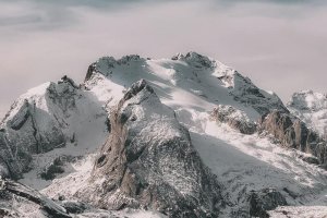 Snow-covered mountain range under cloudy sky Snowy mountain peaks with cloudy sky