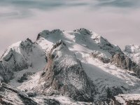 Snow-covered mountain range under cloudy sky Snowy mountain peaks with cloudy sky