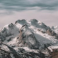 Snow-covered mountain range under cloudy sky Snowy mountain peaks with cloudy sky