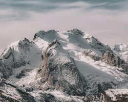 Snow-covered mountain range under cloudy sky Snowy mountain peaks with cloudy sky