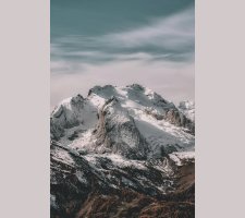 Snow-covered mountain range under cloudy sky Snowy mountain peaks with cloudy sky