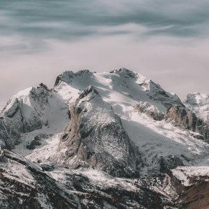 Snow-covered mountain range under cloudy sky Snowy mountain peaks with cloudy sky